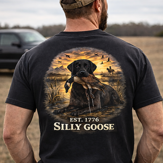 Person wearing a black t-shirt with a graphic of a dog and sunset, featuring the text 'Est. 1776 Silly Goose'.