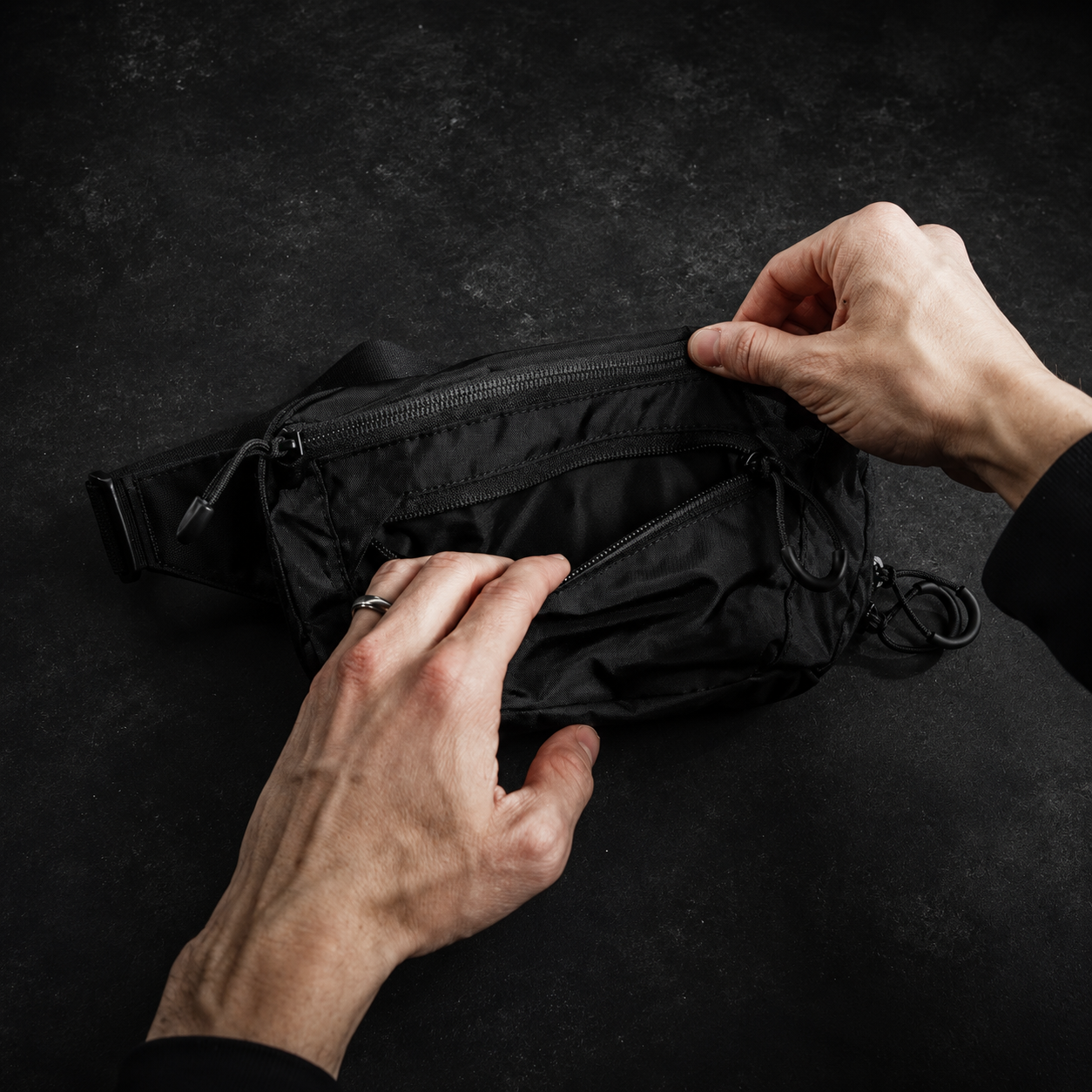Person opening a black waist bag on a dark background
